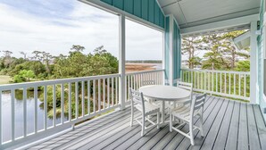 A covered outdoor area with a table and chairs, overlooking a body of water and a natural landscape. - Hamilton Cay Reserve at Bermuda Bay (Kill Devil Hills)