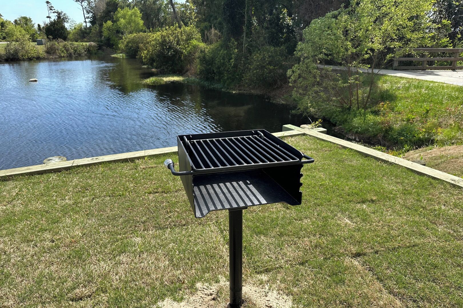 A portable grill set up on a grassy area near a body of water.