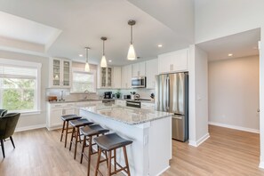 A modern kitchen with a large island, stainless steel appliances, and pendant lighting. - Hamilton Cay Reserve at Bermuda Bay (Kill Devil Hills)