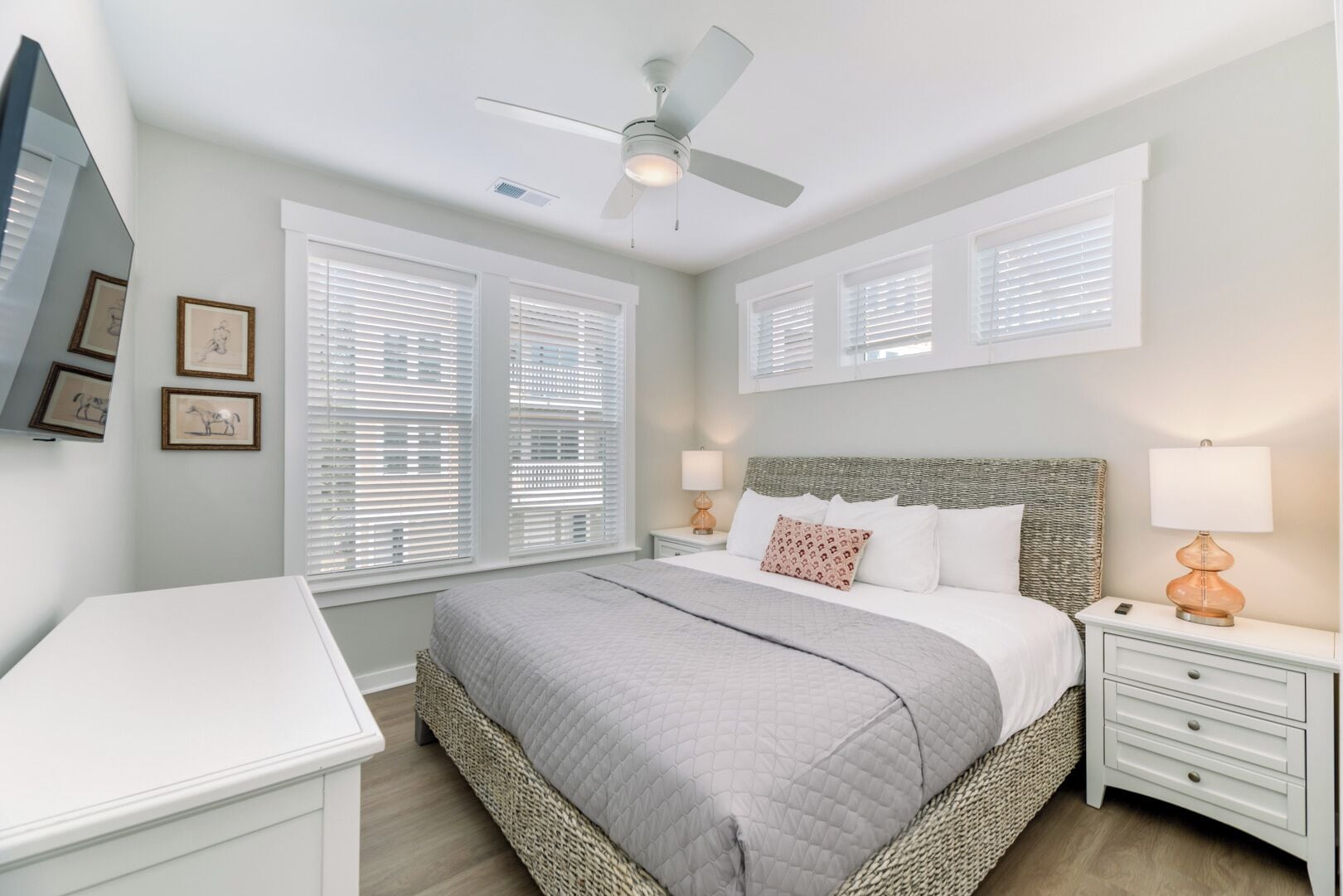 A bedroom with a bed, bedside tables, a ceiling fan, and framed pictures on the wall.