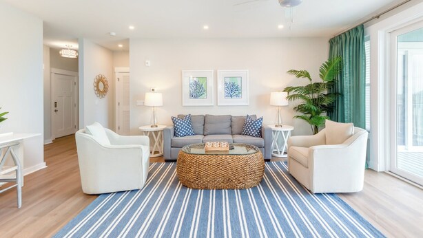 A modern living room with a grey sofa, white armchairs, a woven coffee table, and a ceiling fan. - Hamilton Cay Reserve at Bermuda Bay (Kill Devil Hills)