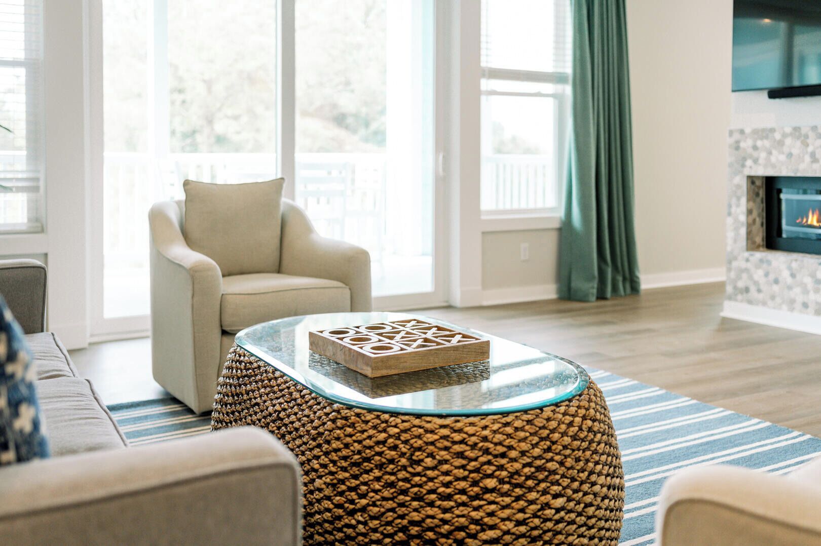 Un salon avec une table basse en verre, un pouf en osier, un fauteuil beige et une cheminée.