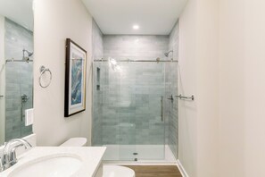 A modern bathroom with a glass-enclosed shower, a white sink, and a framed picture on the wall. - Hamilton Cay Reserve at Bermuda Bay (Kill Devil Hills)