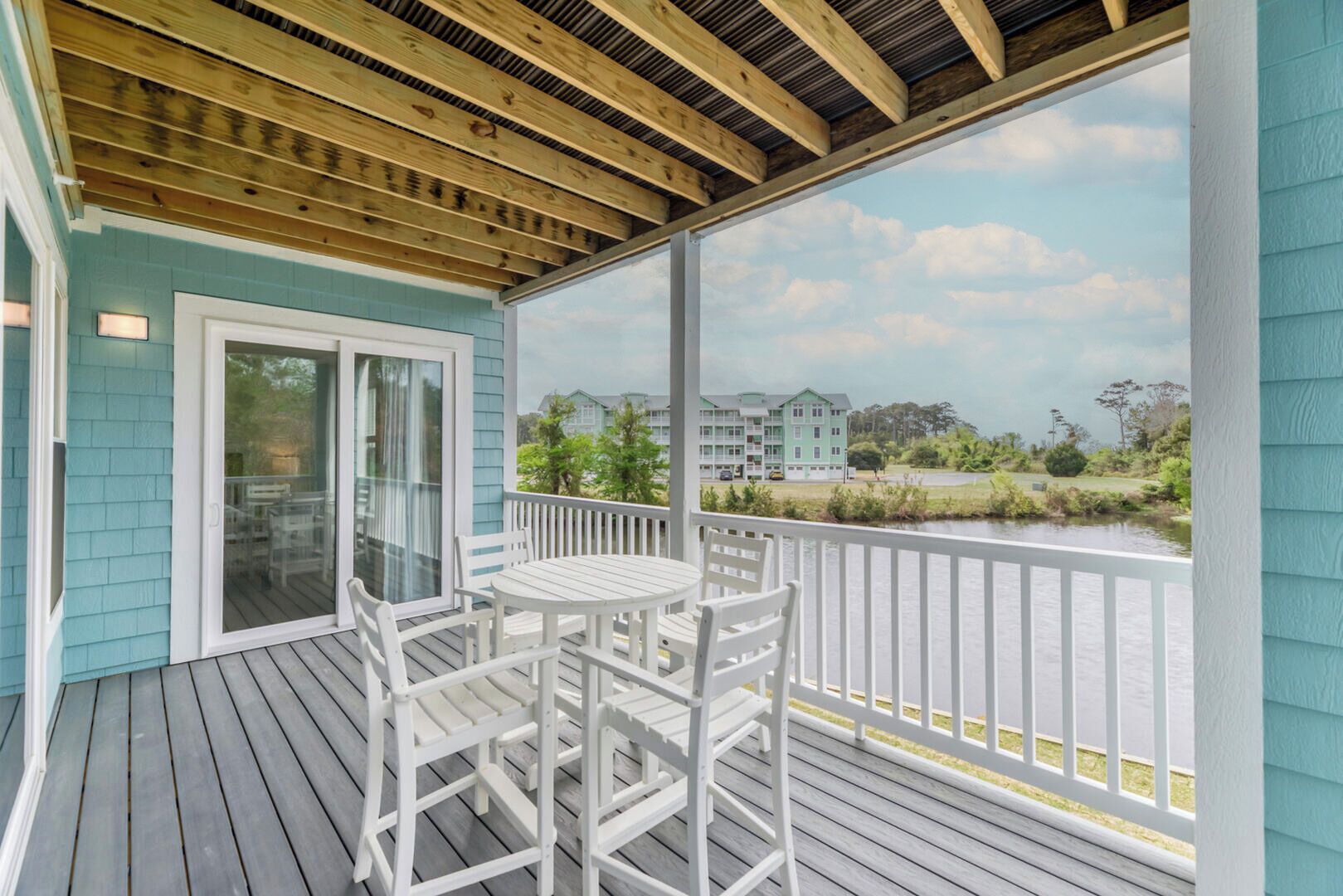 A covered outdoor area with a table and chairs, a sliding glass door, and a view of a water body and buildings in the background.