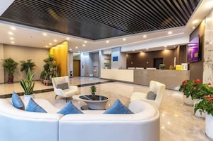 Un moderno vestíbulo de hotel con una recepción, área de descanso y plantas en macetas.