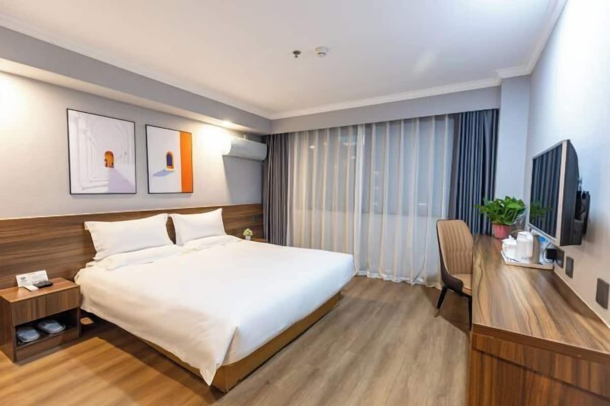 A hotel room with a large bed, a desk, a chair, a TV, and a window with curtains.