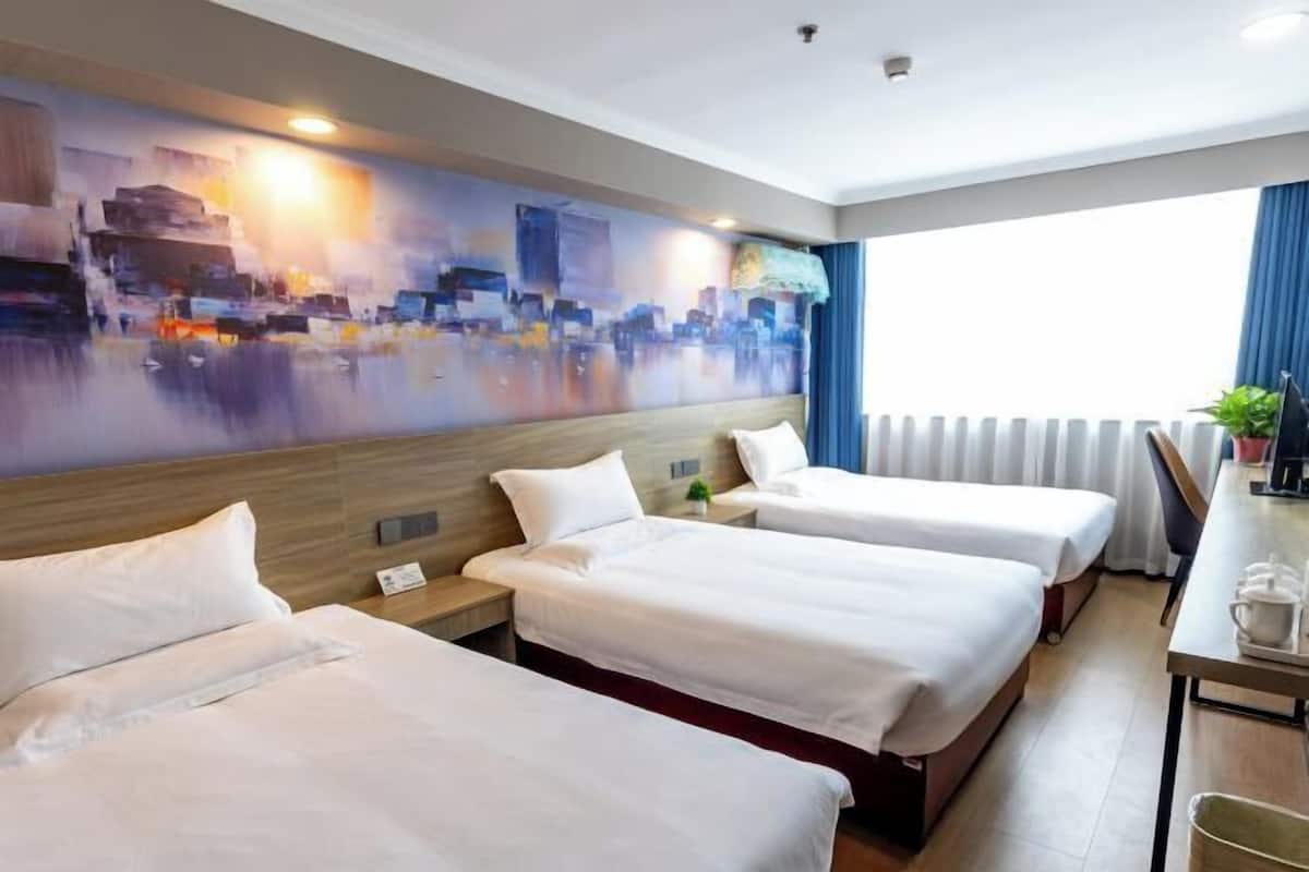 A hotel room with three beds, a desk, and a large cityscape painting on the wall.
