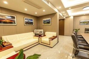 Une chambre d’hôtel moderne avec un canapé, une table à manger et une chaise. Les murs sont ornés de tableaux encadrés et une plante est posée sur la table.