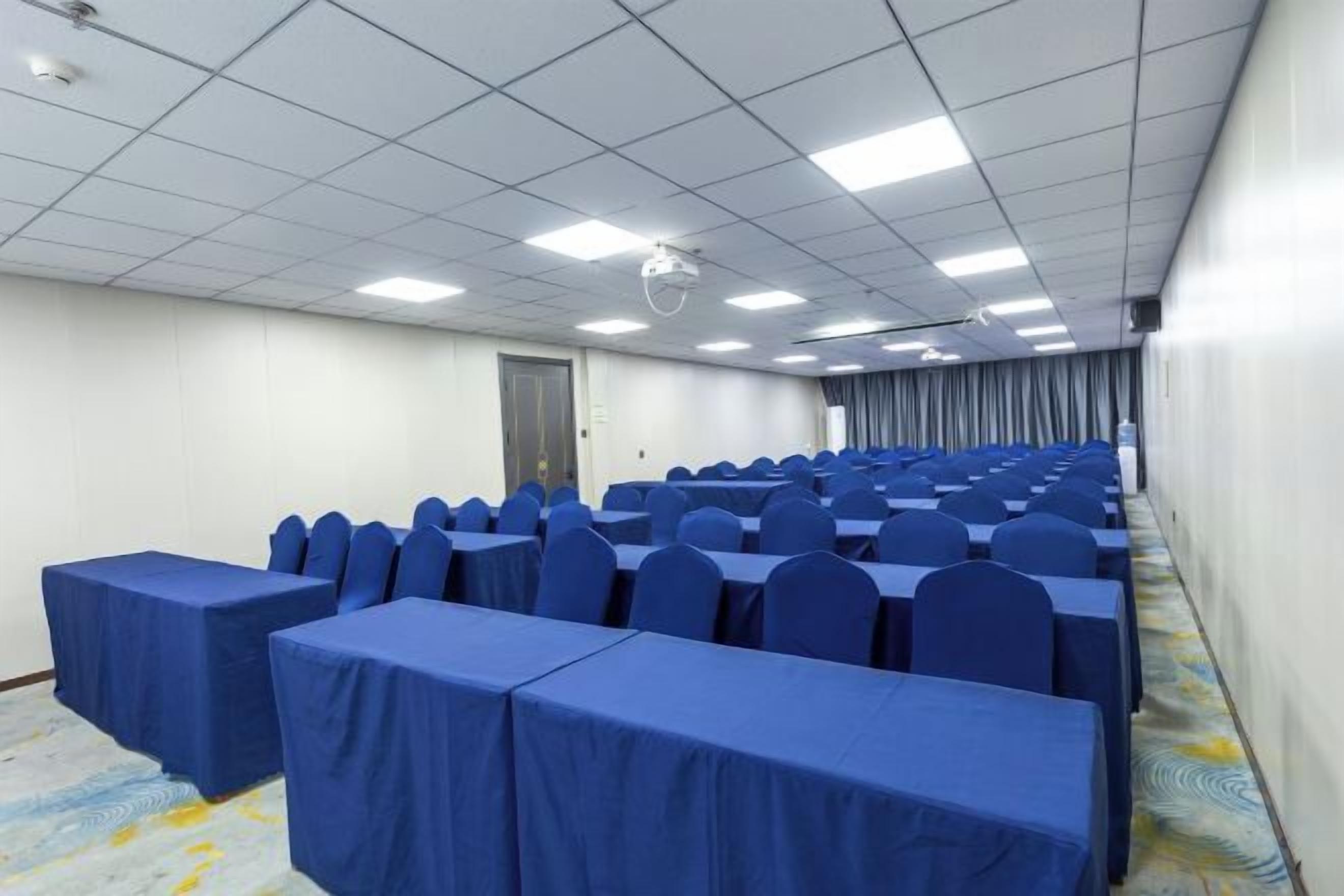 Un salón de conferencias con filas de mesas y sillas, un proyector y una puerta.