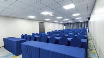 Un salón de conferencias con filas de mesas y sillas, un proyector y una puerta.