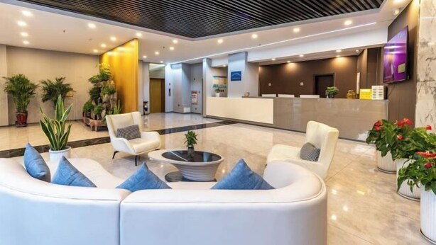 A modern lobby with a reception desk, seating area, and potted plants.