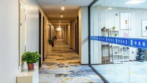 A hotel hallway with a patterned floor, potted plants, and a blue sign with text.