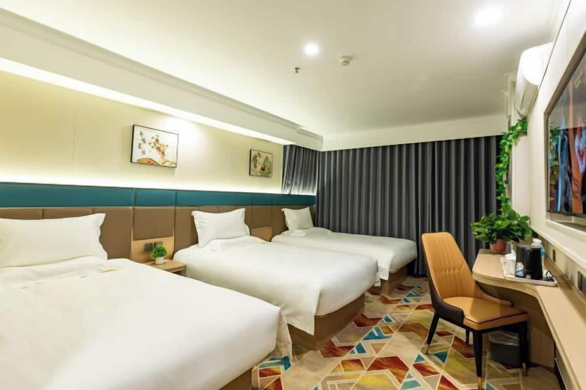 A hotel room with three beds, a desk with a chair, and a TV.