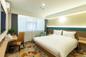 A hotel room with a large bed, a desk, a chair, a small table, a potted plant, and a window with curtains. - ning zhao Hotel (Shijiazhuang Railway University Subway Station) (Shijiazhuang)