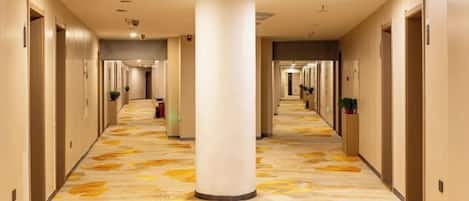 A hotel corridor with a patterned carpet, columns, and doors leading to rooms.