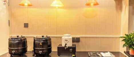 A restroom with three black kettles, a coffee machine, and a trash bin.