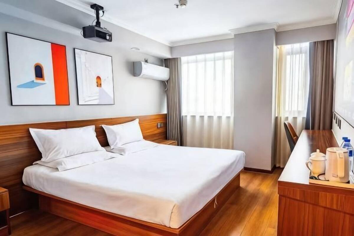 A hotel room with a wooden bed, a desk with a chair, and a large window with curtains.