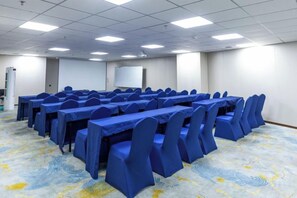 A conference room with multiple tables and chairs, a projector screen, and a carpeted floor. - ning zhao Hotel (Shijiazhuang Railway University Subway Station) (Shijiazhuang)