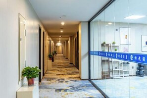 A hotel corridor with a patterned carpet, glass walls, and a blue sign.