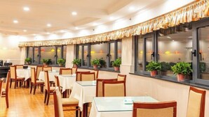 A restaurant with multiple tables and chairs, potted plants on windowsills, and a warm, well-lit interior.
