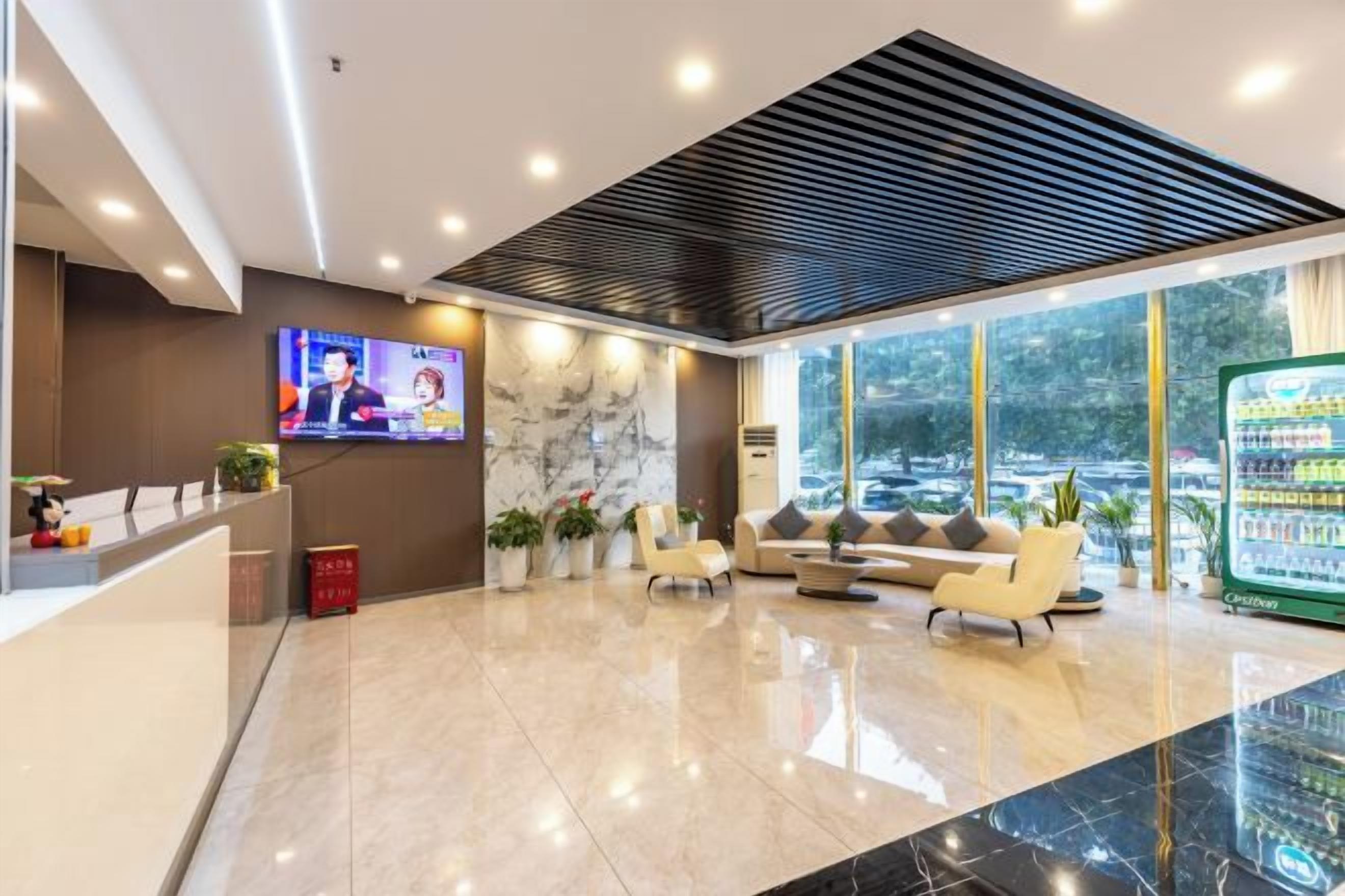 Zona de recepción de un hotel con televisor, asientos y refrigerador.