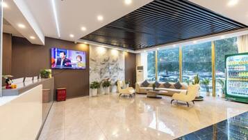 Zona de recepción de un hotel con televisor, asientos y refrigerador.
