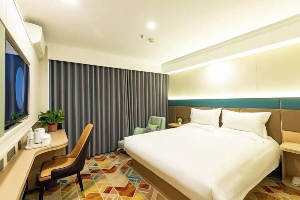 A hotel room with a large bed, a desk with a chair, a television, and a plant.