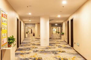 Un couloir d’hôtel avec un sol à motifs, des colonnes et des portes donnant sur les chambres.