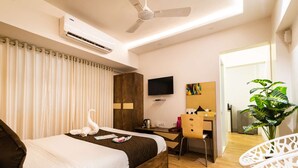 A hotel room with a bed, a desk, a chair, a TV, and a plant. - Deluxe Room with Kitchen (Mumbai)