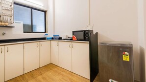 A compact kitchen with white cabinets, a black microwave, and a stainless steel refrigerator. - Deluxe Room with Kitchen (Mumbai)