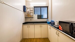 A compact kitchen with white cabinets, a black countertop, a microwave, and a window above the sink. - Deluxe Room with Kitchen (Mumbai)