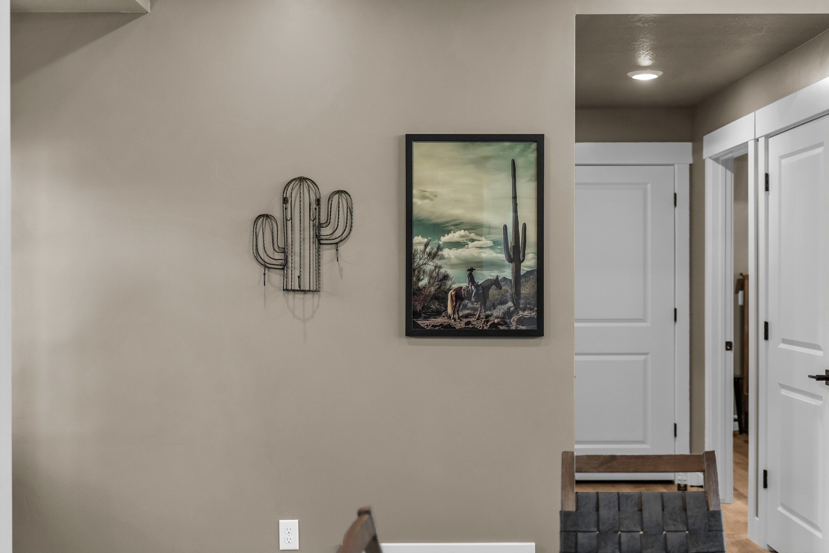Un pasillo con una obra de arte de cactus, un cuadro enmarcado con un paisaje desértico y un banco de madera.
