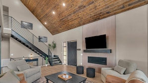 A modern living room with a staircase, a flat-screen TV mounted on the wall, and a coffee table with decorative items.