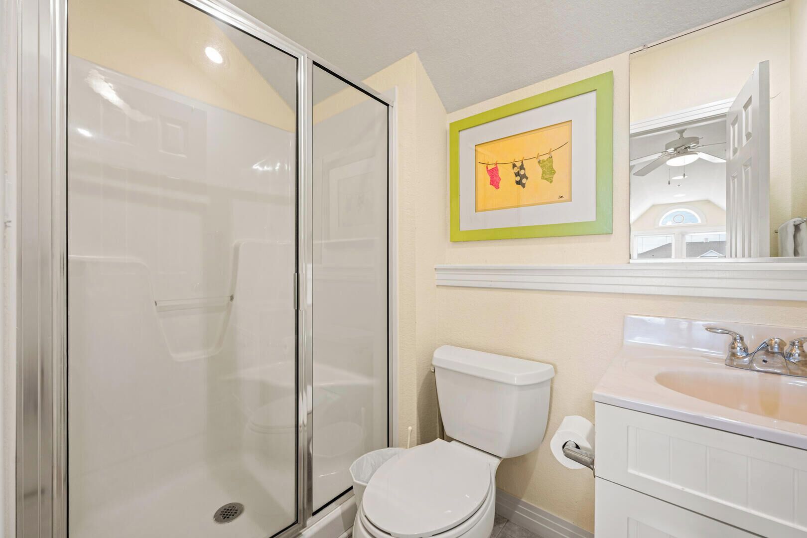 Baño con cabina de ducha de vidrio, inodoro, lavamanos y un cuadro en la pared.
