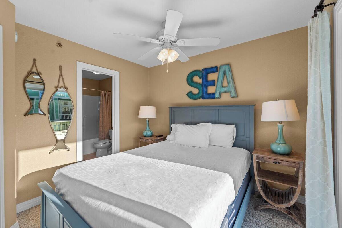 A bedroom with a bed, two nightstands, a ceiling fan, and a wall-mounted word "SEA".