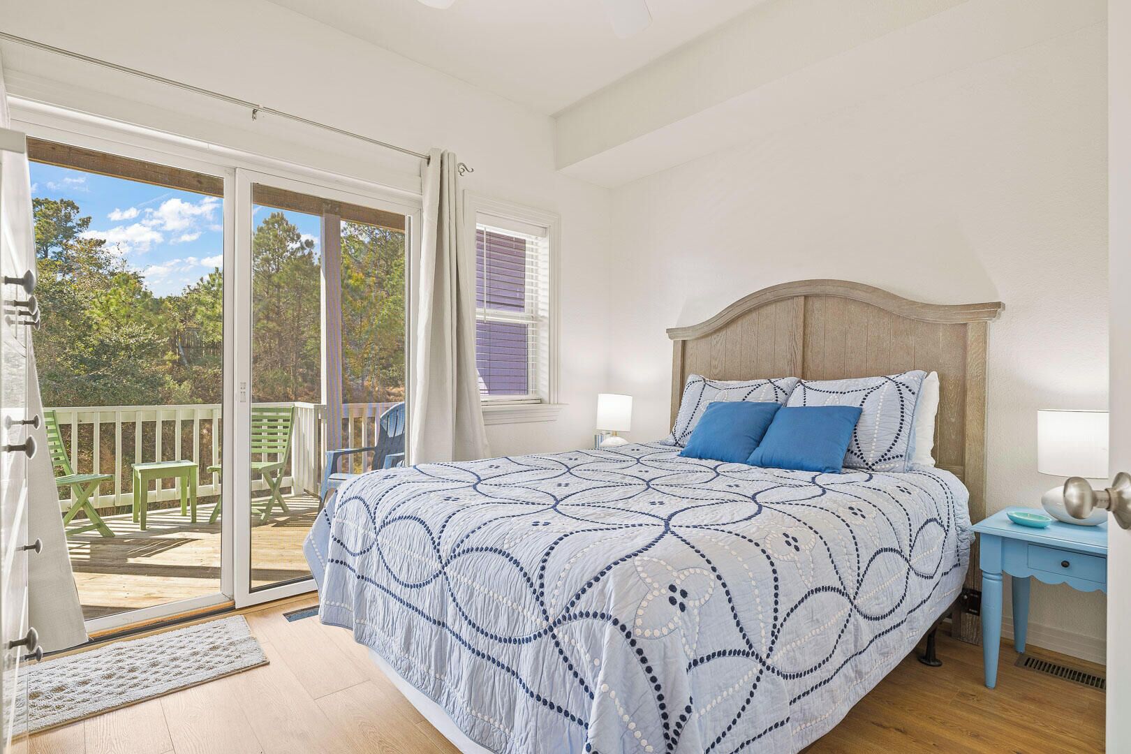 A bedroom with a large bed, a wooden headboard, two bedside lamps, and a view of a deck with outdoor furniture.