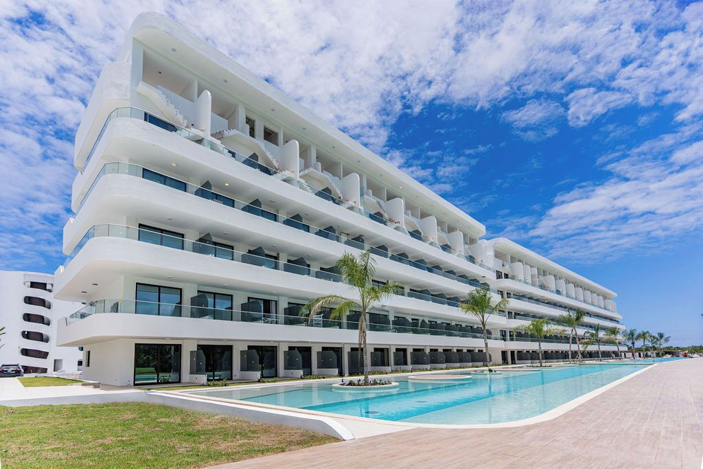 A modern hotel with multiple balconies, a swimming pool, and a clear blue sky.