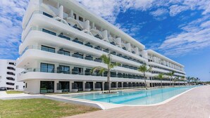 Un hôtel moderne doté de nombreux balcons, d’une piscine et offrant une vue sur un ciel d’un bleu éclatant.