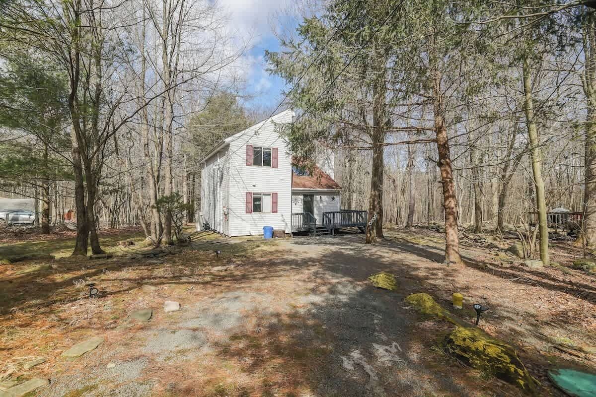 Une maison blanche à deux étages, entourée d’arbres dans une zone boisée.