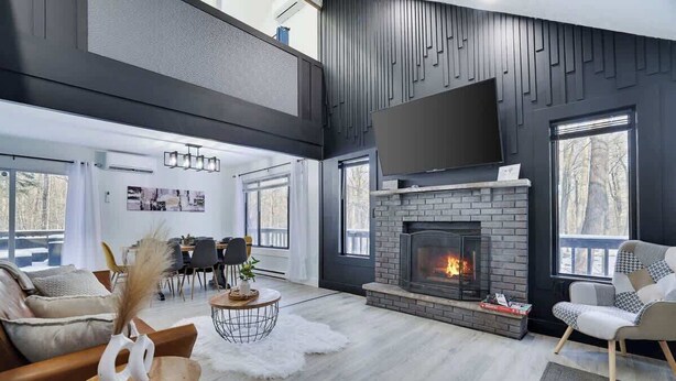 A modern living room with a fireplace, a sofa, a coffee table, and a TV mounted on the wall. - Starlight Chalet | Game Room | Pool Access | AC (Tobyhanna)