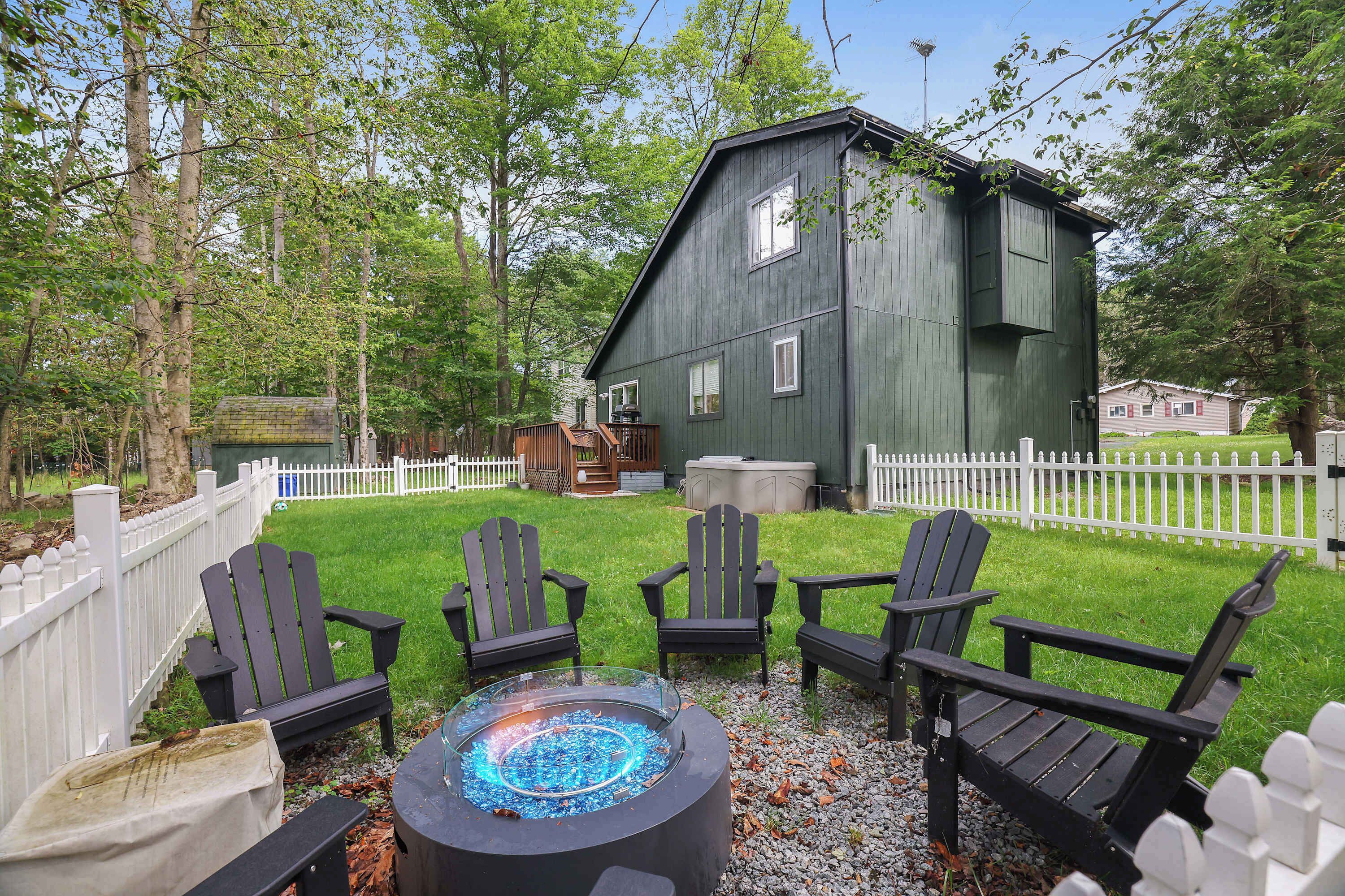 A backyard with a fire pit, four Adirondack chairs, and a wooden deck.