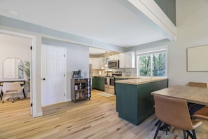 A modern kitchen with a central island, wooden flooring, and a view of the outdoors through large windows.