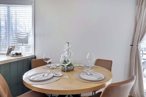 Una mesa redonda para comer con un jarrón de flores blancas, puesta con platos, cubiertos y copas de vino.