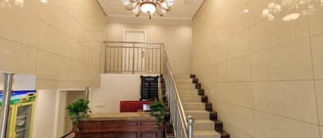 A staircase with a handrail, a reception desk with plants, and a chandelier.