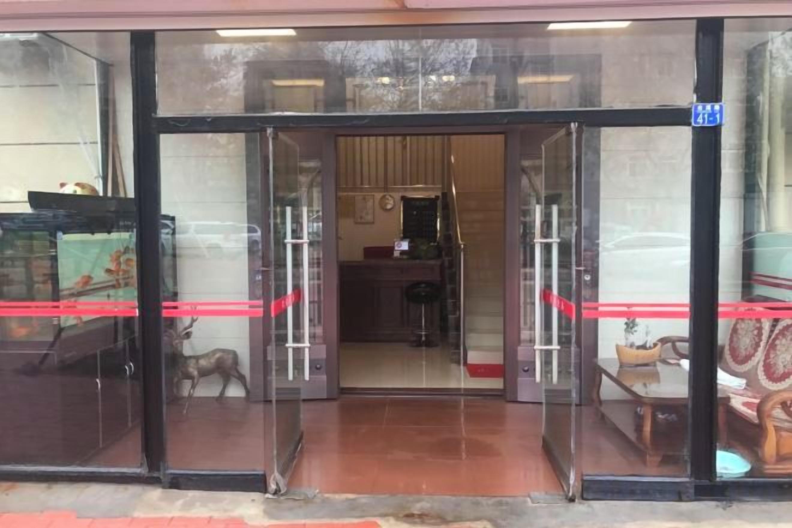 A hotel entrance with glass doors, a visible interior with furniture, and a red ribbon on the door.