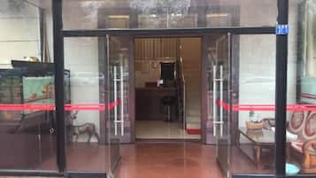 A hotel entrance with glass doors, a visible interior with furniture, and a red ribbon on the door.