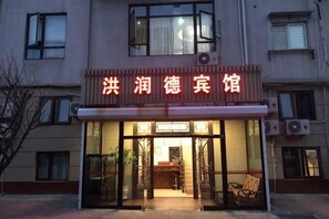 L’entrée d’un hôtel, avec une enseigne, des portes vitrées et un espace extérieur aménagé avec des sièges.