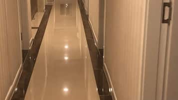 A corridor with a reflective floor and walls, leading to a door at the end.
