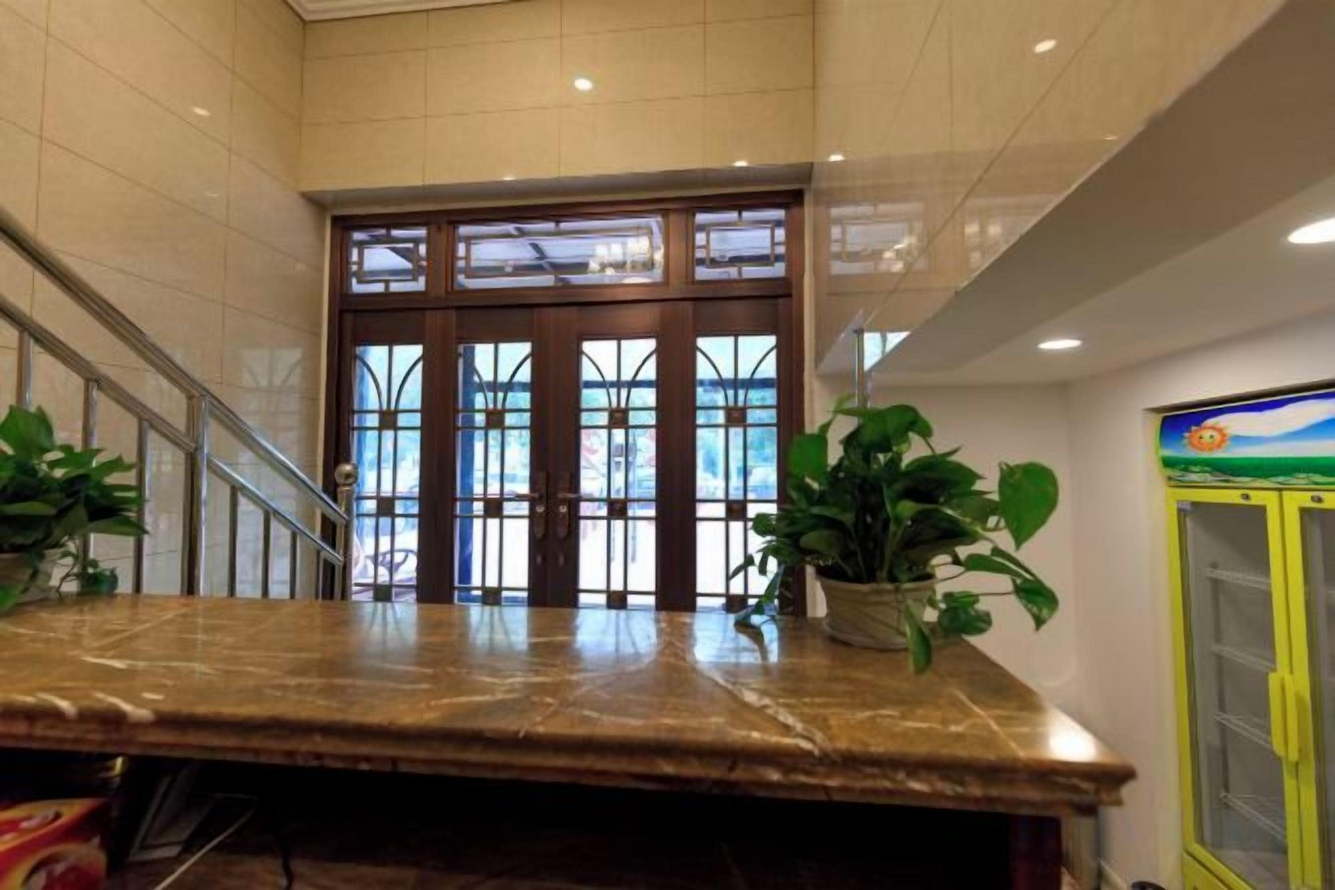 Un hall d’entrée avec un comptoir de réception en marbre, un escalier et une porte d’entrée en verre.
