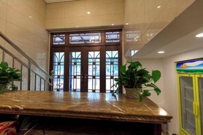 Un hall d’entrée avec un comptoir de réception en marbre, un escalier et une porte d’entrée en verre.